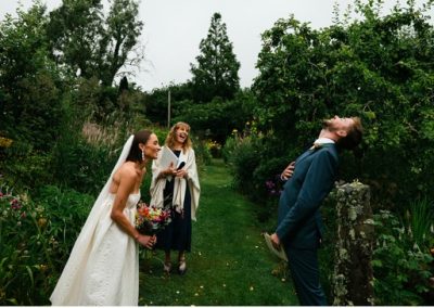 The bride, groom and celebrant laugh uproariously in a garden ceremony