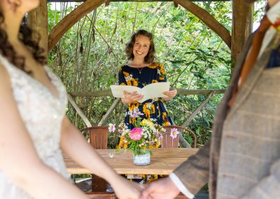 Celebrant in a sunflower pattern dress in pergola with couples hands and flowers in front