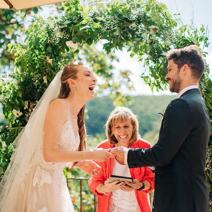 wedding celebrant in south of France between laughing bride and groom with flower arch behind